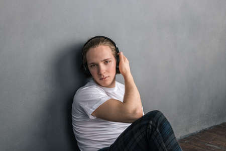 Handsome young man sitting on the floor in living room, having headphones on his headの写真素材