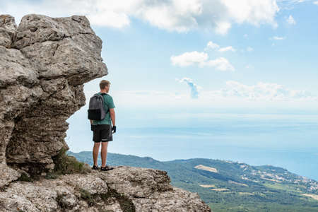 Young man on top of cliff in mountains and enjoying view of nature