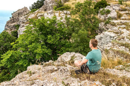 Young man practicing yoga pose sitting on the rocky peak