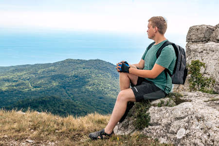 Young man on top of cliff in mountains and enjoying view of natureの写真素材