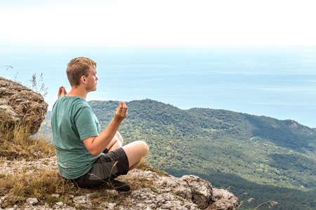 Young man practicing yoga pose sitting on the rocky peakの写真素材