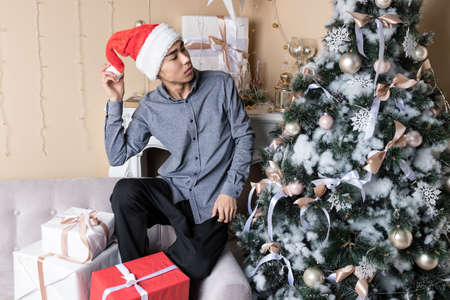 Young man in santas hat sitting on couch near christmas tree and fireplaceの写真素材