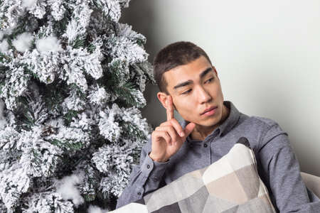 Young happy man sitting on couch near christmas treeの写真素材