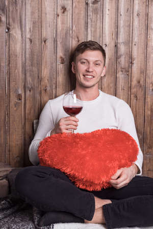 Young handsome man with a glass of wine sitting near wood wallの写真素材