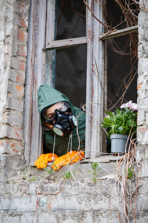 A man in a raincoat and gas mask collects a flower from a scorched, poisonous earth. Air pollution concept. Ecological catastrophe.の写真素材