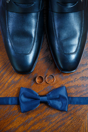 gold wedding rings lie on the table next to the men's bow tie and shoesの写真素材