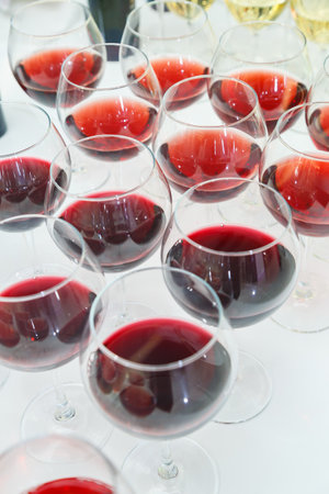A large number of glass goblets filled with red wine are neatly arranged on the banquet table for the celebration. Wine is a type of alcoholic beverage.の写真素材