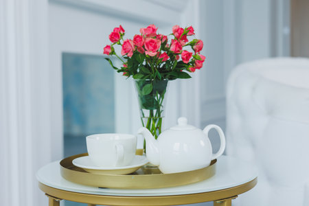 A table with a white teapot and a white cup. on the table a vase with fresh flowersの写真素材
