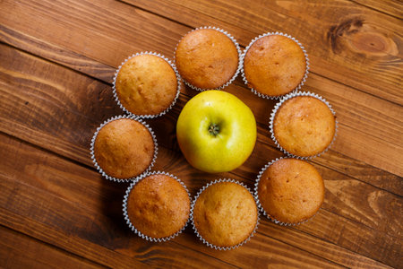 Homemade muffins in a paper wrap with an apple on a wooden boardの写真素材