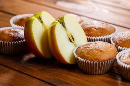 Homemade muffins in a paper wrap with an apple on a wooden boardの写真素材