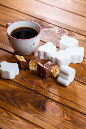 white cup of black coffee, chocolate with nuts on a wooden board with marshmallowsの写真素材