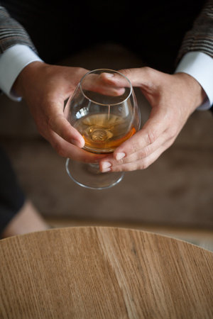 A man businessman holds a glass with alcohol in his hand. Dressed in a jacket and shirt. Rest after...