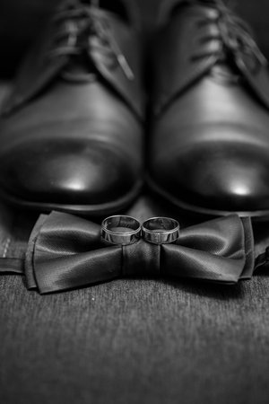 gold wedding rings lie on the table next to the men's bow tie and shoesの写真素材