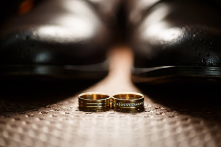 Gold wedding rings of the newlyweds lie next to men's shoes for the groomの写真素材