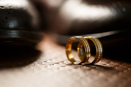 Gold wedding rings of the newlyweds lie next to men's shoes for the groomの写真素材