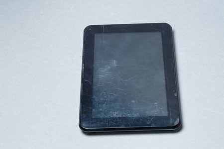 Black scratched tablet with a protective film on a gray background. Protect your device screenの写真素材