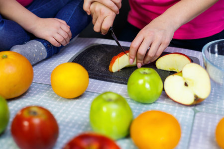 daughter and mom cut a fruit salad consisting of apple orange and mandarin