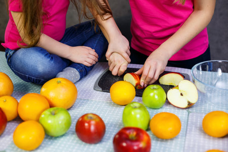 daughter and mom cut a fruit salad consisting of apple orange and mandarinの写真素材