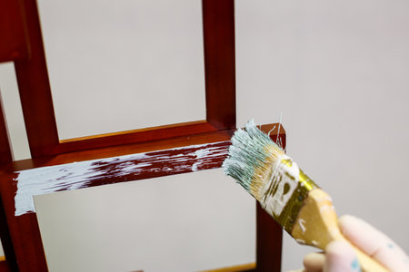 the master paints with a brush a wooden brown photo frame with light paintの写真素材