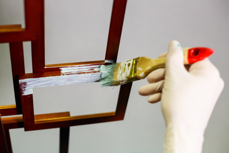 the master paints with a brush a wooden brown photo frame with light paintの写真素材