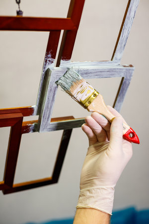 the master paints with a brush a wooden brown photo frame with light paintの写真素材