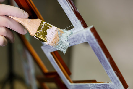 the master paints with a brush a wooden brown photo frame with light paintの写真素材