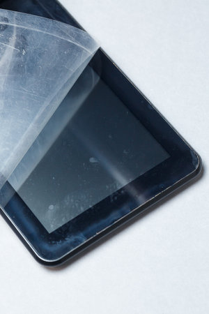 Black scratched tablet with a protective film on a gray background. Protect your device screen