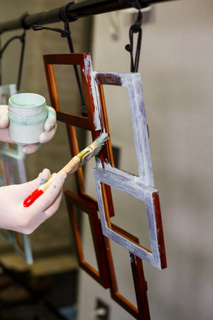 the master paints with a brush a wooden brown photo frame with light paintの写真素材