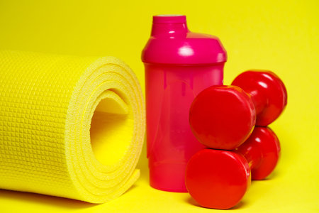 red dumbbells, pink shaker, yellow mat, colored background, sports, energy drink, gym equipmentの写真素材