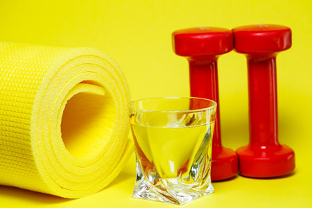 red dumbbells, a glass of water, a yellow rug, colored background, sports, energy drink, equipment for the gymの写真素材