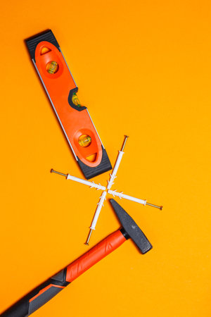 Tools for repair. Hammer for nails, level, dowel in the wall on an orange background. Toolkit for the wizardの写真素材