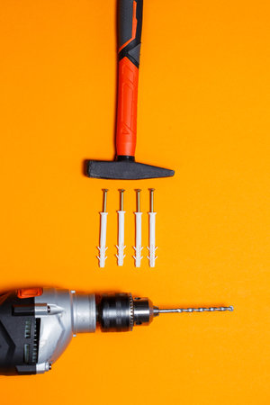 Tools for repair. Hammer for nails, drill, dowel in the wall on an orange background. Toolkit for...