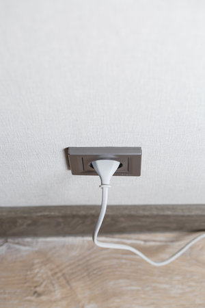 A gray outlet on the wall which includes a device with a white cord. Charging from a power outlet