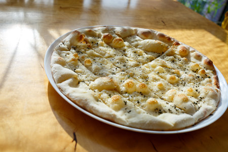 large freshly baked pizza with spices sprinkled with cheese in bright sunlightの写真素材