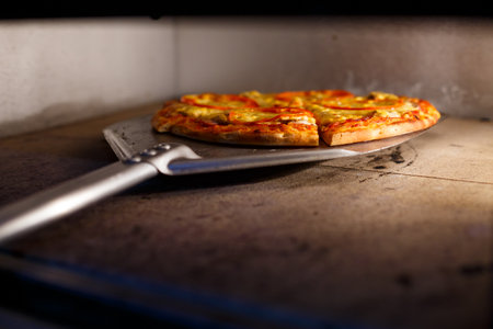 Hot tasty American pizza with tomato cheese and meat with a thick crust on a metal shovel, the baker takes out the pizza from the ovenの写真素材