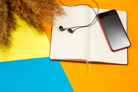 A notebook with clean white sheets for recording with a pen on a colored background, a telephone and headphones, crumpled dry branches nearby. Record, report, message, letter. Place for textの写真素材