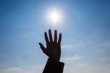 silhouetted a female hand against a blue sky and bright sunの写真素材