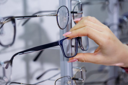 Row of glasses at an opticians. Eyeglasses shop. Stand with glasses in the store of optics. Woman's hand shows glasses. Presenting spectacles. Closeupの写真素材