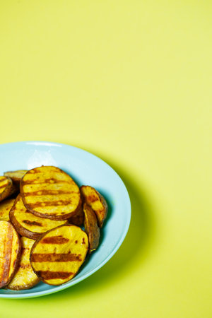 grilled potatoes until golden brown in a blue plate on a yellow backgroundの写真素材