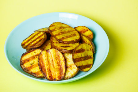 grilled potatoes until golden brown in a blue plate on a yellow backgroundの写真素材
