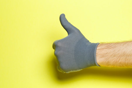 hand of a man, craftsman, gardener in a gray glove on a yellow backgroundの写真素材