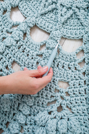 Women's hands lie on a plaid of coarse knitted wool on a wooden floor, top view. Handmade carpetの写真素材