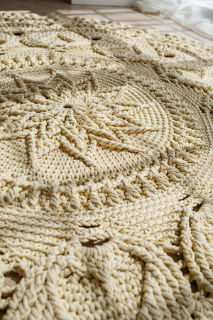 Homemade knitted carpet made of thick threads, made by hand: a handmade rug made of beige threads lies on the floor, the sun shines on itの写真素材