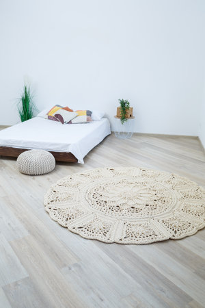 Cute homemade knitted pattern of thick threads made by hand: a handmade rug made of beige threads lies in the bedroom near the bed, the art of knittingの写真素材