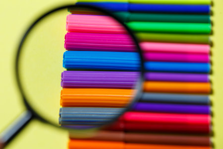 multi-colored markers for drawing through a magnifying glass on a yellow backgroundの写真素材
