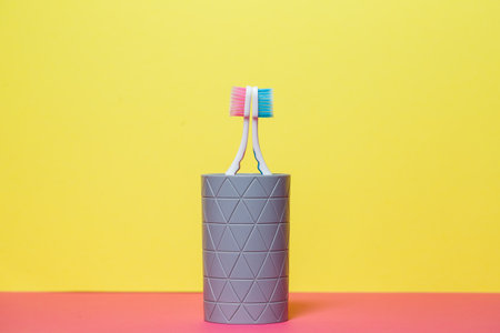 Two toothbrushes stand with a gray glass on a yellow background. Toothbrush concept for a couple,...
