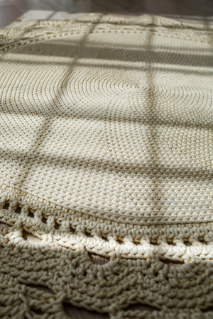 Homemade knitted carpet made of thick threads, made by hand: a handmade rug made of beige threads lies on the floor, the sun shines on itの写真素材
