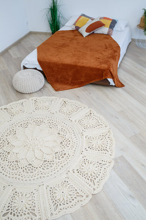 Cute homemade knitted pattern of thick threads made by hand: a handmade rug made of beige threads lies in the bedroom near the bed, the art of knittingの写真素材