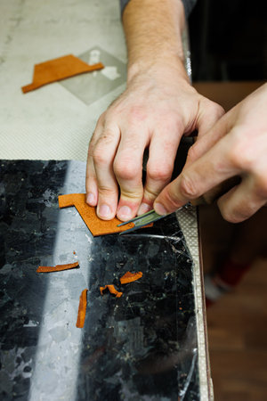 A man's hand holds pieces of leather for a leather wallet in his workshop. The process of working with natural brown leather. The craftsman holds the craftの写真素材