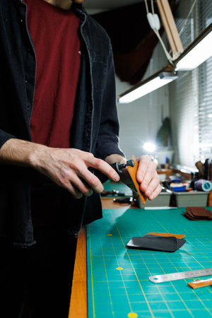A man's hand holds pieces of leather for a leather wallet in his workshop. The process of working...